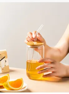 Detailed view of clear glass cup with wooden lid, glass straw, and fresh drink inside.