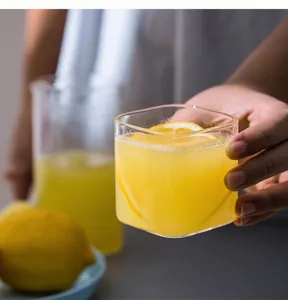 Detailansicht des quadratischen Glases mit frischem Saft und Zitrone in Alltagsszene.
