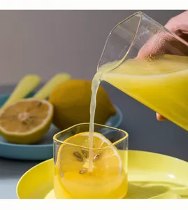 Detailierte Nahaufnahme eines quadratischen Glaskrugs, der frischen Saft in ein Glas gießt.