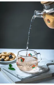 Primo piano dettagliato della tazza in vetro con fragole e teiera che versa tè rinfrescante.
