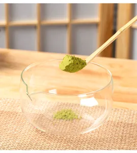 Clear glass matcha bowl detail with bamboo scoop and green powder in traditional tea setting.