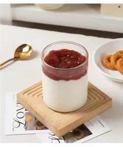 Vue détaillée d'une tasse à pudding en verre transparent avec yaourt sur un sous-verre en bois.