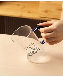 Close-up view of clear glass coffee mug featuring dark blue handle and stylish printed text.