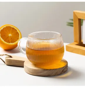 Detailed view of transparent ribbed glass cup with warm tea on wooden coaster prop.