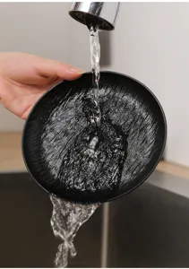 Nahaufnahme Detailansicht eines schwarzen strukturierten Knochentellers unter fließendem Wasser.