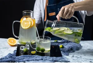 Vue détaillée de la carafe d'eau en verre résistant à la chaleur avec tasse et fruits.