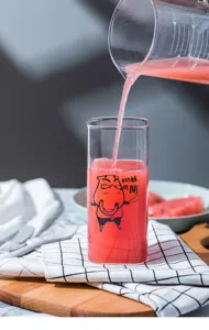 Detail shot of transparent glass square cup with creative funny cartoon print pouring juice.