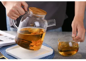 Borosilicate glass teapot with wooden lid pouring tea detail, heat-resistant clear water kettle.