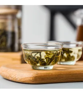 Detail shot of clear heat-resistant glass tea cup with brewed green tea on wooden tray.