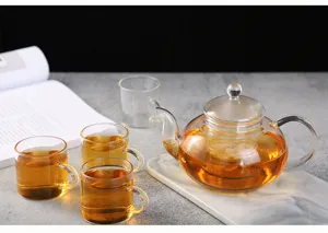 Vue détaillée d'une théière en verre résistante à la chaleur avec filtre sur plateau.