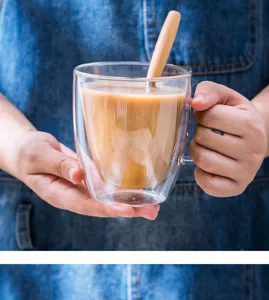 Nahaufnahme einer klaren doppelwandigen Glastasse mit Kaffe und Holzlöffel Detail.
