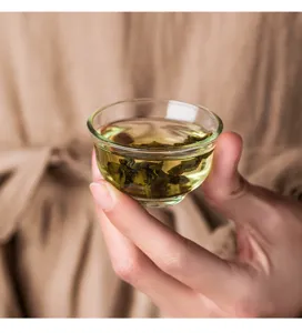 Detailed view of clear glass tea tasting cup filled with freshly brewed green tea leaves.