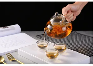 Théière en verre transparente versant du thé parfumé dans trois tasses à double paroi.