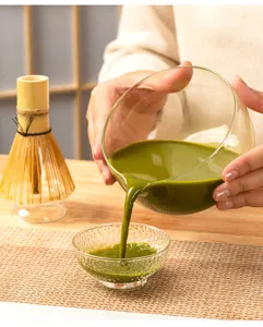 Close-up detail of pourable glass matcha bowl and bamboo whisk set for traditional tea whisking.