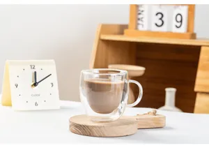 Nahaufnahme eines doppelwandigen Glasbechers auf einem Holzuntersetzer mit Kaffee.