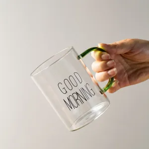Clear glass coffee mug with green handle and printed text, transparent breakfast cup main view