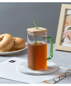 Detailed close-up shot of a square glass cup featuring a green handle, wooden lid and straw.