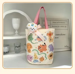 Primer plano detallado del bolso de lona con animales, asas rosas y colgante de peluche.