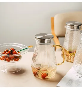 Close-up detail of heat-resistant glass water pitcher with golden handle and steel lid.