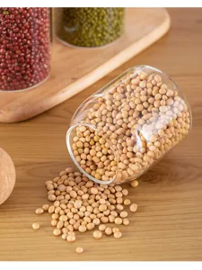 Clear glass storage jar detail showcasing spilled soybeans on wooden table for kitchen grain display.