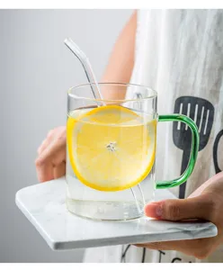Primo piano di tazza in vetro trasparente con manico verde e cannuccia per bevande rinfrescanti.