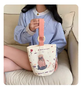 Casual canvas bucket handbag with wooden ring handle and cute cartoon graphic design.