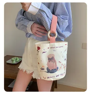 Close-up of canvas bucket bag with cute girl print, wooden ring handle and pink strap.