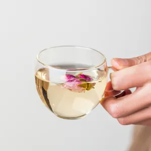 Clear borosilicate glass tea cup with handle holding warm tea and a pink flower bud.