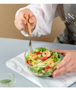 Glass salad bowl detail showing convenient pour spout design with fresh food and wooden fork.