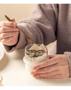 Glazen yoghurtbeker met lepel toont havermout en fruit detail in levensstijl.