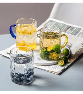 Primo piano di tazze in vetro lavorato e bicchieri d'acqua con frutta e vassoio di marmo