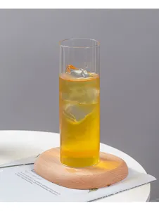 Detailaufnahme des klaren geraden Glasbechers mit goldenem Getränk auf einem Holzuntersetzer.