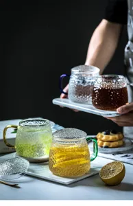 Detail shot of hammered glass tea cup with lid and handle, elegant lifestyle tableware setup.