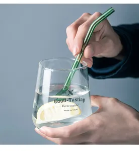 Close-up detail shot of transparent glass cup with green bent straw and lemon slice.