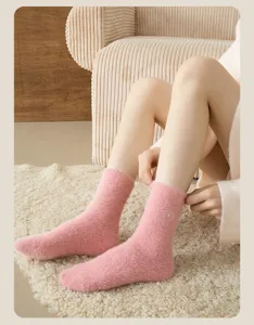Close-up detail of cozy pink fuzzy mid-tube sleep socks with cute heart embroidery on soft rug.