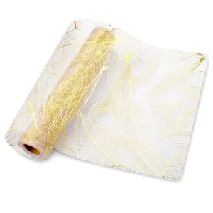 Détail rapproché du motif de feuilles dorées sur chemin de table en maille blanche.