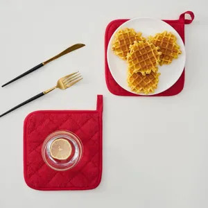Close-up detail of red quilted kitchen potholder with hanging loop on white background.