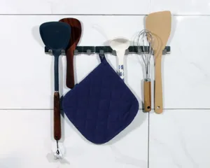 Detail shot of kitchen pot holder and hanging cooking utensils on white tile wall.
