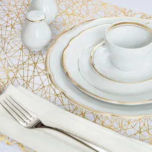 Set di stoviglie in ceramica bianca elegante con bordo dorato e un runner da tavola geometrico.