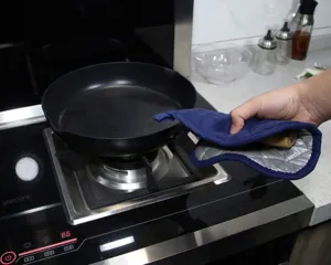 Close-up detail of blue kitchen heat-resistant oven mitt with silver lining during cooking.