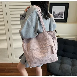 Vista laterale di una grande borsa tote in tela rosa con tasche laterali, indossata da una modella