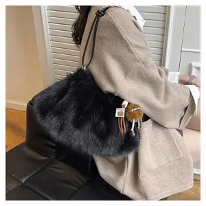 Stylische schwarze flauschige Kunstfell-Achseltasche mit braunem Plüschanhänger an der Schulter