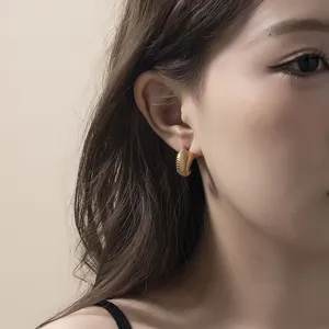 Gros plan détaillé de boucles d'oreilles créoles dorées et côtelées portées par modèle.