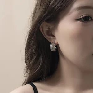 Gros plan détail de boucles d'oreilles créoles argentées texturées portées à l'oreille.