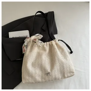 Detailed shot of a chic straw woven shoulder bag with lace ribbon and metal bow detail.