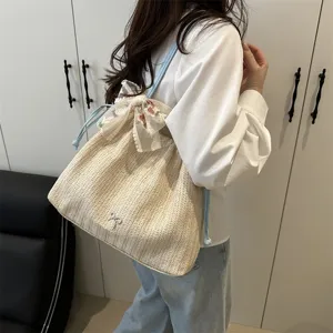 Detailed shot of women's woven straw shoulder tote bag with cute lace floral bow and blue straps.