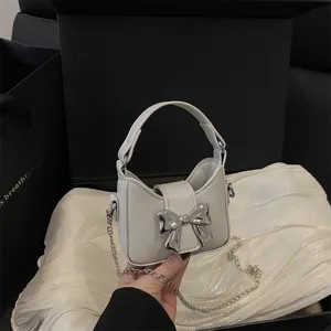 Detail view of a cute white toddler handbag featuring a metallic bow and chain strap design.
