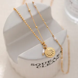 Chaîne de clavicule élégante avec pendentif coquillage, perles d'eau douce et design métallique.
