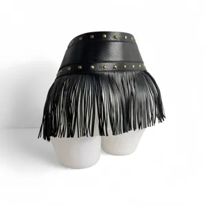 Close-up detail of the wide black waist belt featuring metallic pyramid studs and long fringe.