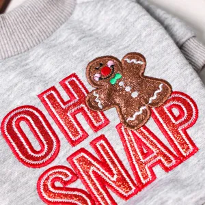 Close up of grey pet sweater detail featuring cute gingerbread man embroidery and bold text.